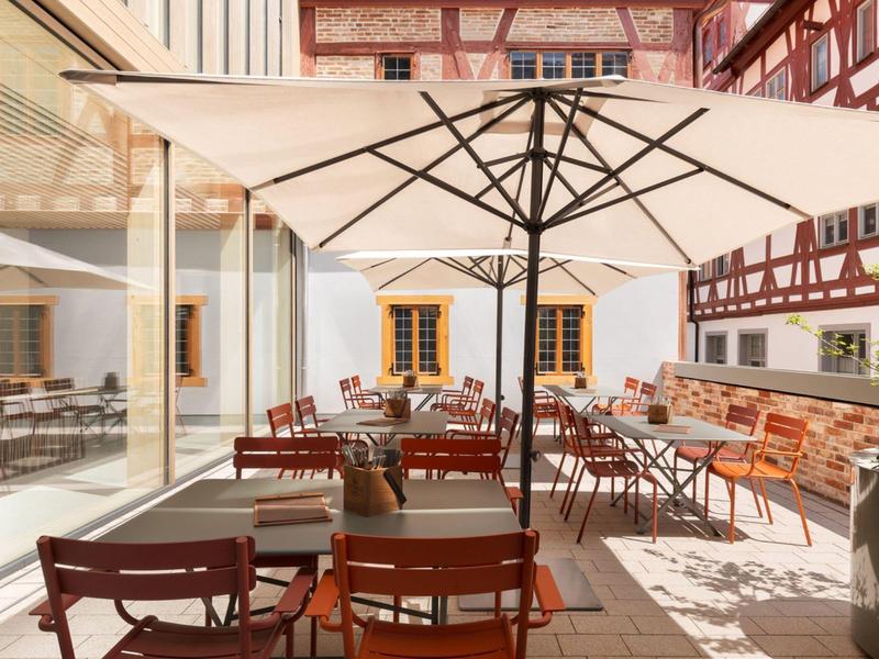 Zonnig buitenterras van een hotel met tafels, stoelen en grote parasols.