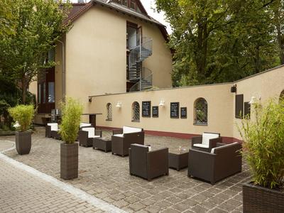 Zewnętrzny teren hotelu z nowoczesnymi siedzeniami i roślinami na brukowanej powierzchni.