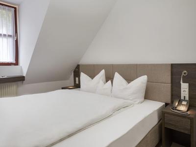 Nowoczesny pokój hotelowy z dużym łóżkiem pod skośnym sufitem i stolikiem nocnym z telefonem.