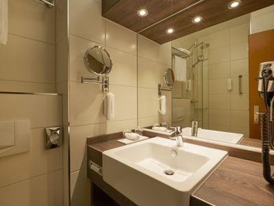 Nowoczesna łazienka hotelowa z podwójną umywalką, lustrem i prysznicem z drzwiami przeszklonymi.