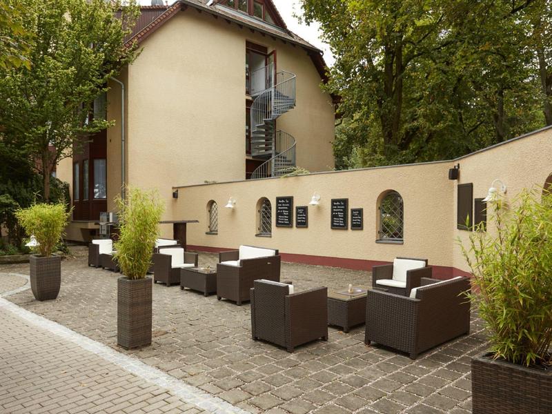 Przestrzeń na zewnątrz hotelu z nowoczesnymi siedzeniami i roślinami wzdłuż ścieżki.