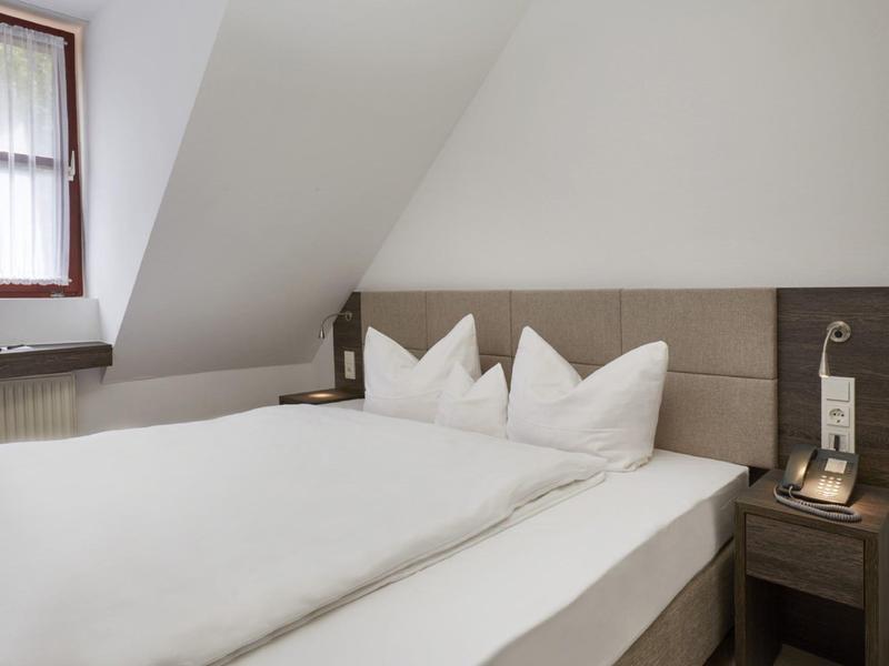 Nowoczesny pokój hotelowy z podwójnym łóżkiem, białą pościelą i stolikiem nocnym pod oknem.