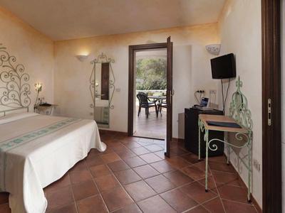 Helles Hotelzimmer mit Doppelbett, Fliesenboden und Blick auf sonnige Terrasse und Grün.