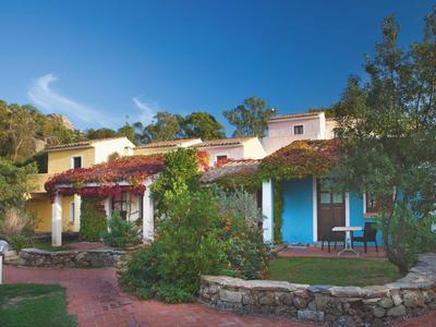 Einfarbiges Haus mit rotem Dach, blauen Türen und üppigen grünen Pflanzen im Garten.