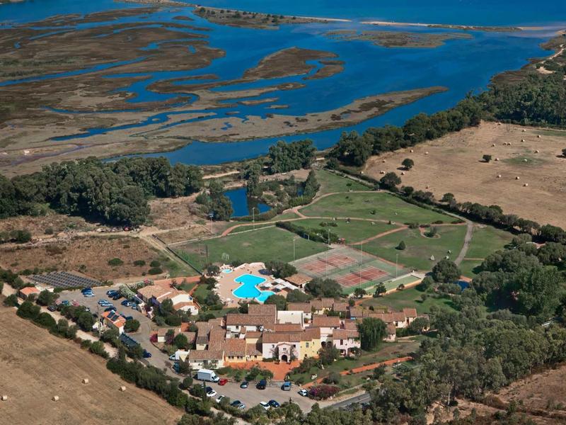 Landschaft mit Feldern, Bäumen und einem Dorf mit blauem Pool in der Mitte, umgeben von Wasserflächen.