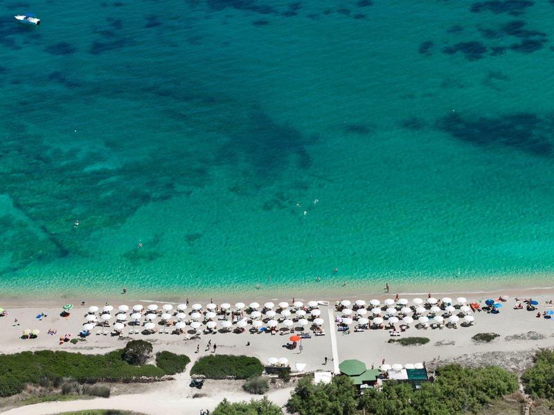 Strand mit weißen Sonnenschirmen und türkisfarbenem Wasser, Vogelperspektive am Hotelurlaubsort.