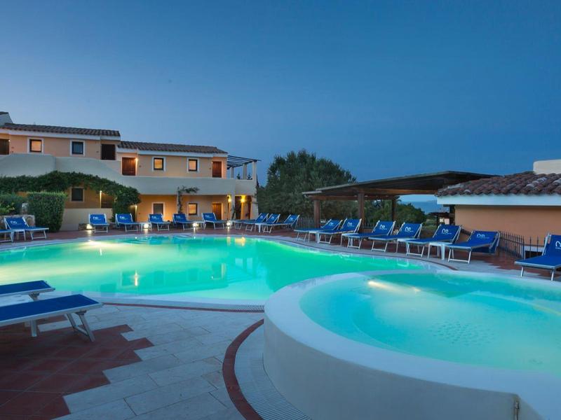 Beleuchteter Poolbereich mit Liegestühlen vor einem Hotel bei Abenddämmerung.