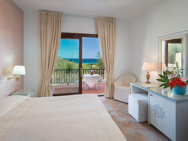 Helles Hotelzimmer mit Doppelbett, Balkon und Blick auf das Meer bei strahlendem Sonnenschein.