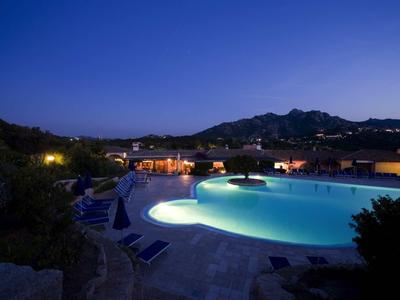 Beleuchteter Pool in ruhiger Landschaft bei blauem Abendhimmel und Bergen im Hintergrund.
