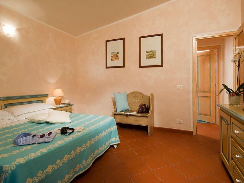 Gemütliches Schlafzimmer mit Doppelbett, kleiner Sitzbank, TV und warmem Licht an beige Wand.