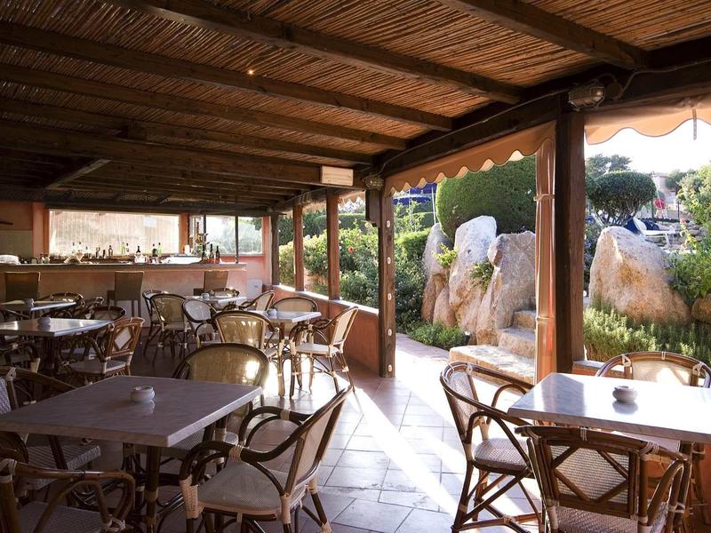 Offener, überdachter Außenbereich mit Holzdach, Tischen und Stühlen, umgeben von Natur und Felsen.