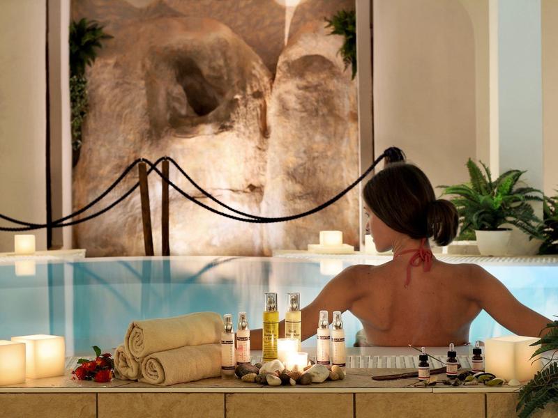 Eine Frau entspannt sich in einem Pool mit Kerzen und Getränken am Rand.