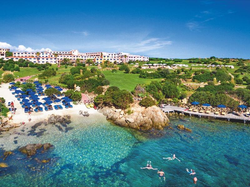 Hotelanlage mit Strand, Liegestühlen und klarem Wasser an einer Felsküste