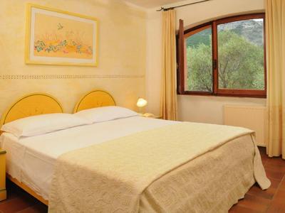 Hell eingerichtetes Schlafzimmer mit großem Bett, gelben Möbeln und Fenster mit Blick ins Grüne.