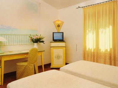 Helles Hotelzimmer mit zwei Betten, gelben Vorhängen und Schreibtisch vor einer Wandmalerei.