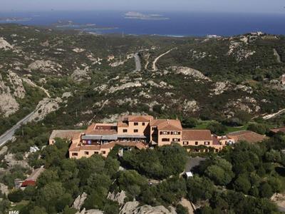 Große Villa mit roten Dächern in grünem Hügelgebiet nahe Küste und Meer im Hintergrund.