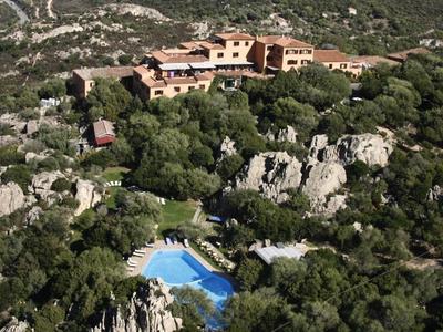 Großes Haus in Felsenlandschaft mit dichten grünen Bäumen und blauem Schwimmbecken.