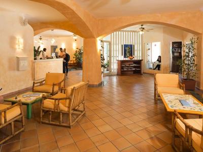 Weitläufiges, lichtdurchflutetes Wohnzimmer mit Terrakottaboden, gelben Sofas und Holzmöbeln.