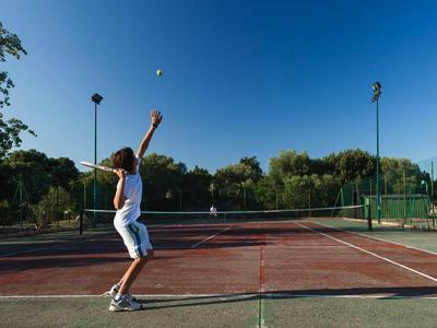 Ein Tennisspieler in weißer Kleidung wirft den Ball für einen Aufschlag auf einem roten Außenplatz.