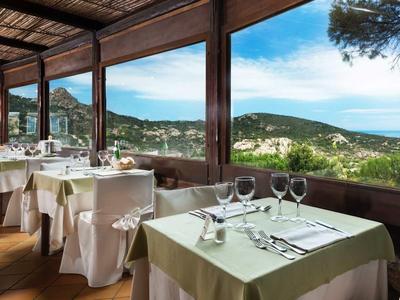 Restaurant mit gedeckten Tischen und Panoramablick auf Hügel und Meer.