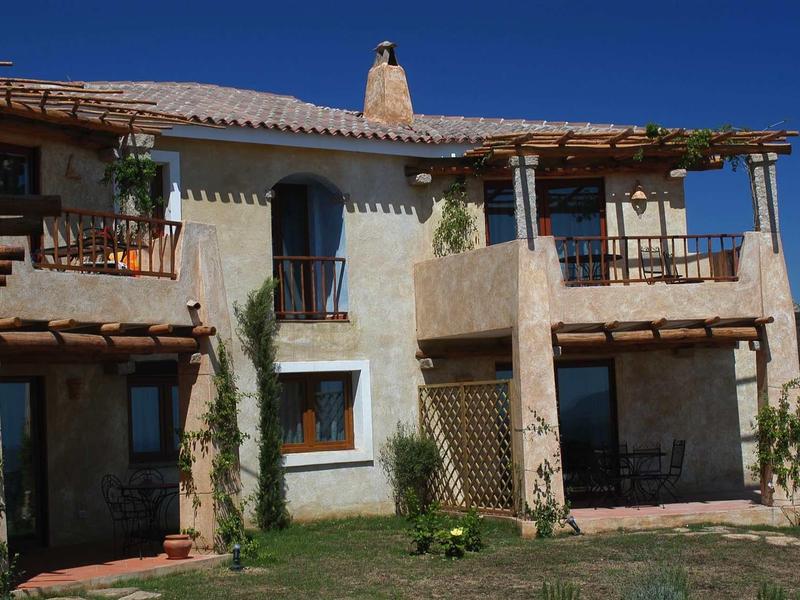 Zweistöckiges Haus mit weißen Wänden, braunen Holzbalkonen und grünem Garten bei klarem Himmel.