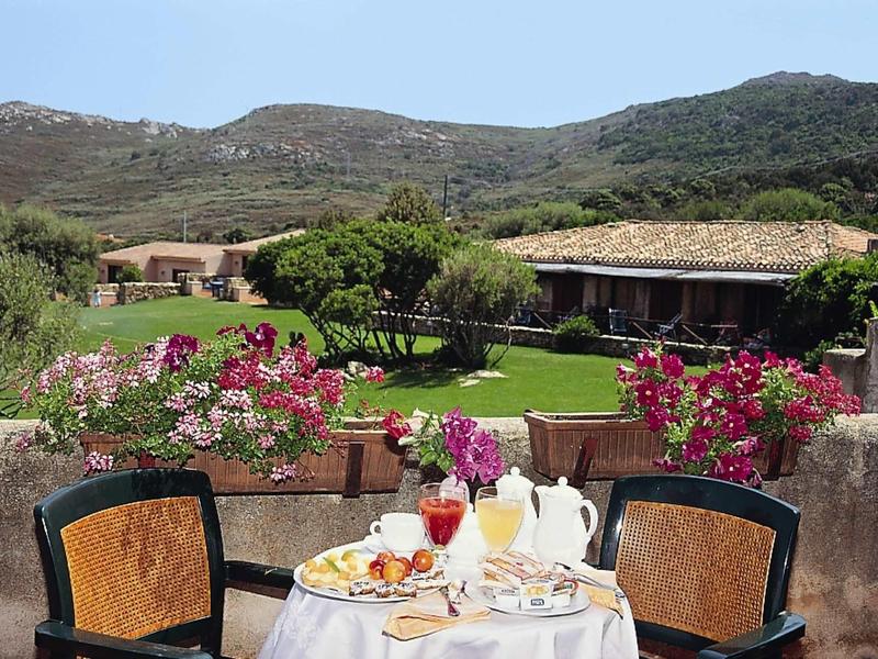 Gedeckter Tisch mit Frühstück vor grünem Garten und Hügeln unter blauem Himmel.
