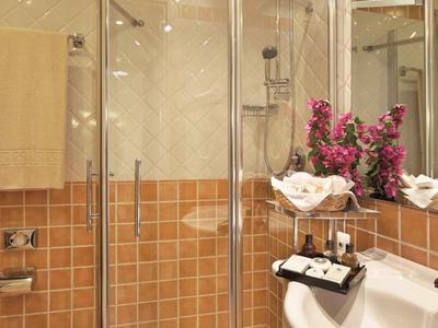 Moderne Badezimmer mit Glasdusche, braun-beigen Fliesen und weißen Handtüchern mit Blumen.