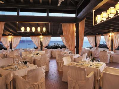 Elegantes Restaurant mit weißen gedeckten Tischen, Stühlen und warmem Licht unter Holzbalken.