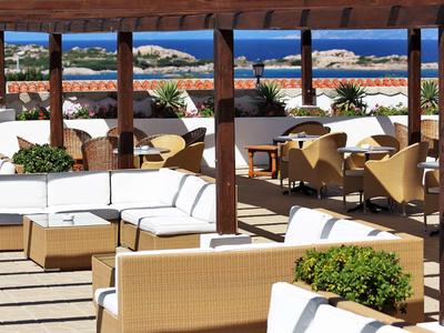 Offener Terrassenbereich mit Holzbalken, weißen Sofas und braunen Stühlen, Meerblick im Hintergrund.