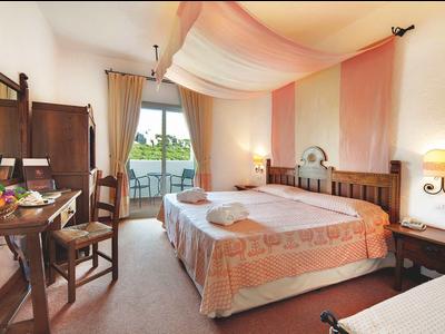 Gemütliches Hotelzimmer mit Doppelbett, Holzmöbeln und Balkon mit Blick ins Grüne.