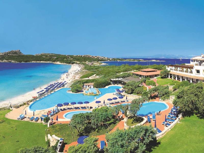 Blick auf Küste mit Hotelanlage, mehreren Pools, grünem Rasen und klarem blauem Meer.