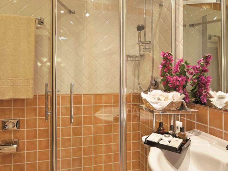 Moderne Badezimmer mit Glasdusche, braun-beigen Fliesen und weißen Handtüchern mit Blumen.