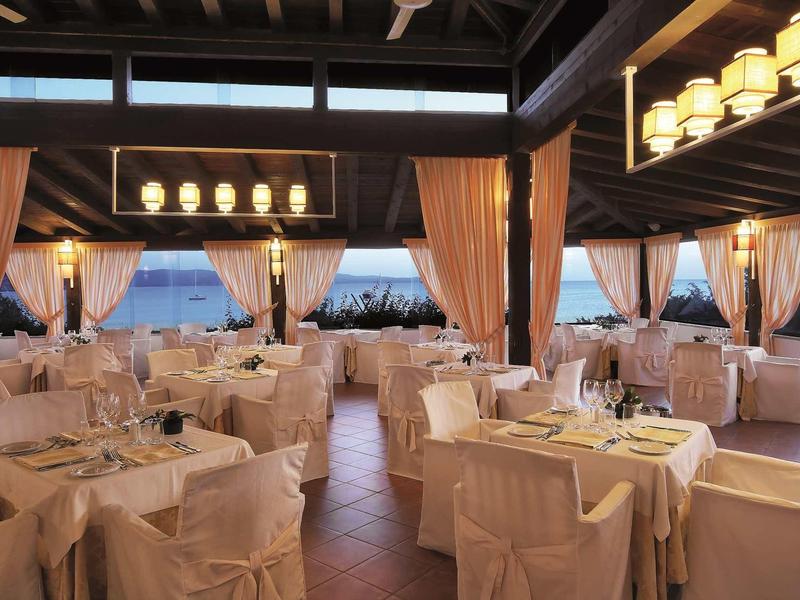 Elegantes Restaurant mit weißen gedeckten Tischen, Stühlen und warmem Licht unter Holzbalken.