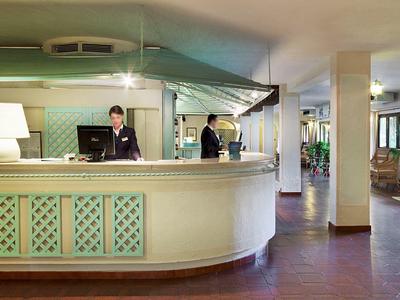 Rezeption eines Hotels mit zwei Mitarbeitern hinter dem Empfangstresen und Sitzbereich im Hintergrund.