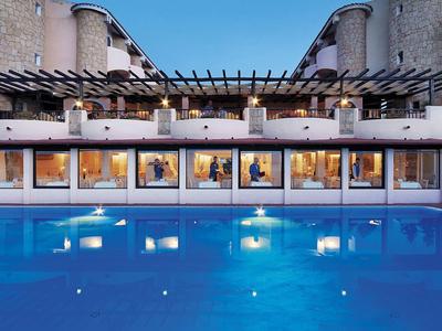 Beleuchteter Pool in der Abenddämmerung vor einem Hotelgebäude mit großen Fenstern.