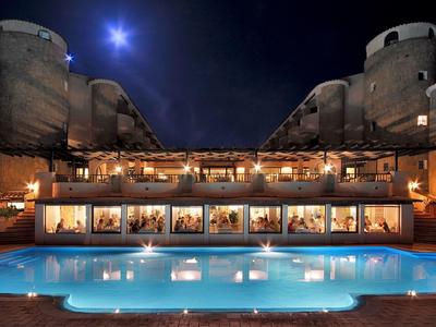 Beleuchteter Pool vor einem historischen Gebäude bei Nacht unter hellem Mondlicht.