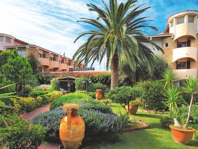 Hotelgebäude mit üppigem Garten und großen Tontöpfen unter blauem Himmel.