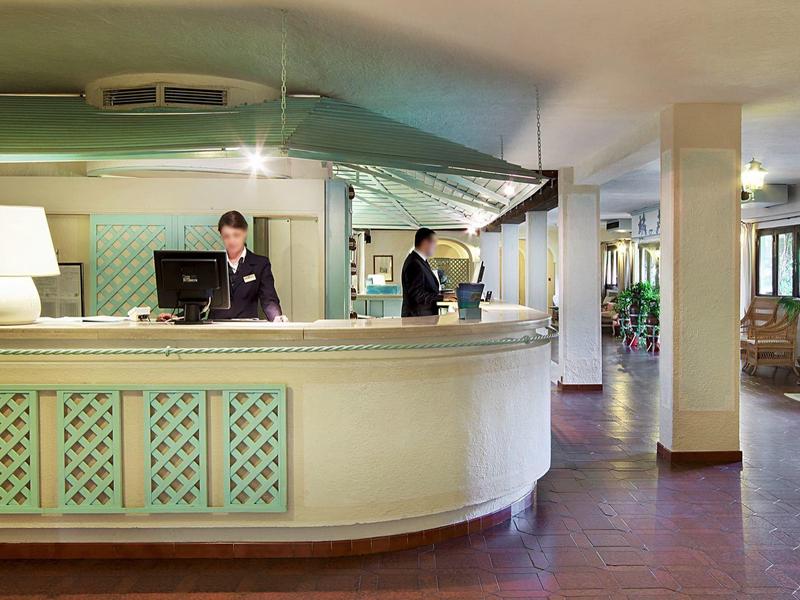 Rezeption eines Hotels mit zwei Mitarbeitern hinter dem Empfangstresen und Sitzbereich im Hintergrund.