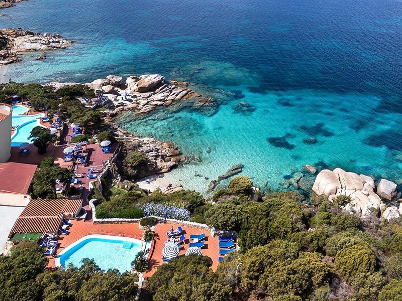 Hotelanlage an der Küste mit Pool, umgeben von Bäumen und klarem blauem Meerwasser.