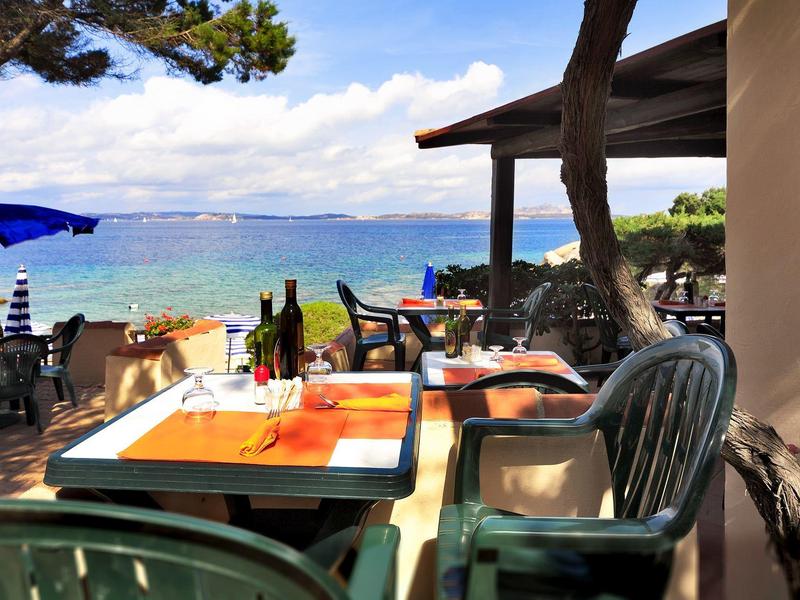 Terrasse mit Tischen und Stühlen mit Blick auf das Meer bei sonnigem Wetter.