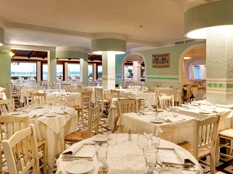 Helles Restaurant mit weißen Tischen und Stühlen, dekoriert für ein Essen mit Blick auf das Meer.