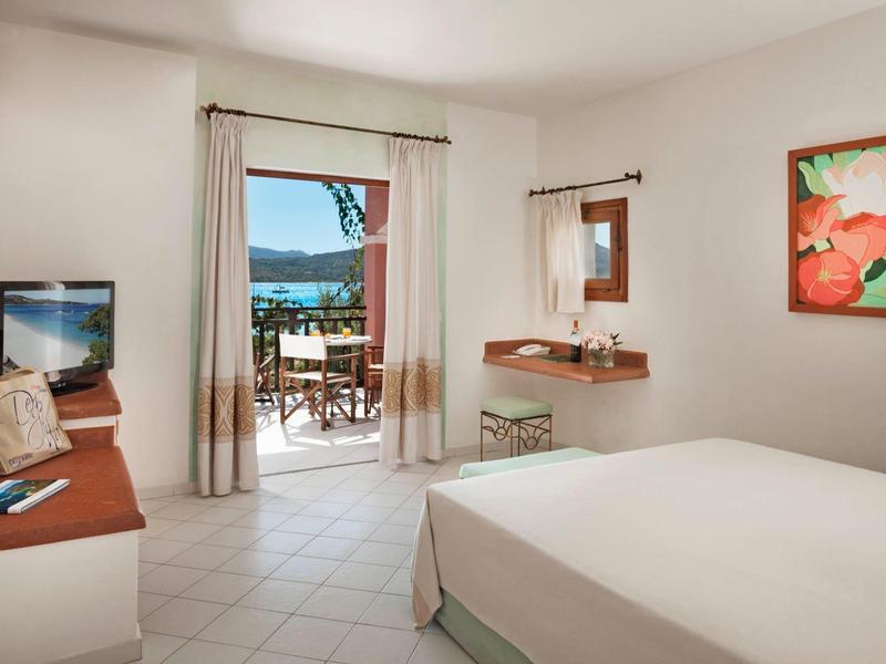 Helles, modern eingerichtetes Schlafzimmer mit Doppelbett, TV, Schreibtisch und Terrasse mit Blick aufs Wasser.