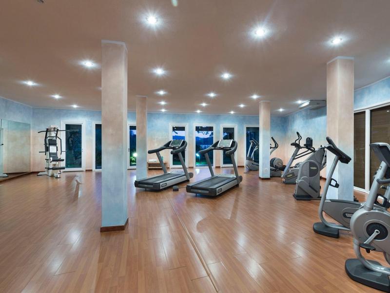 Großer, heller Fitnessraum mit Holzfußboden, Spiegeln, Laufbändern und Ergometern.