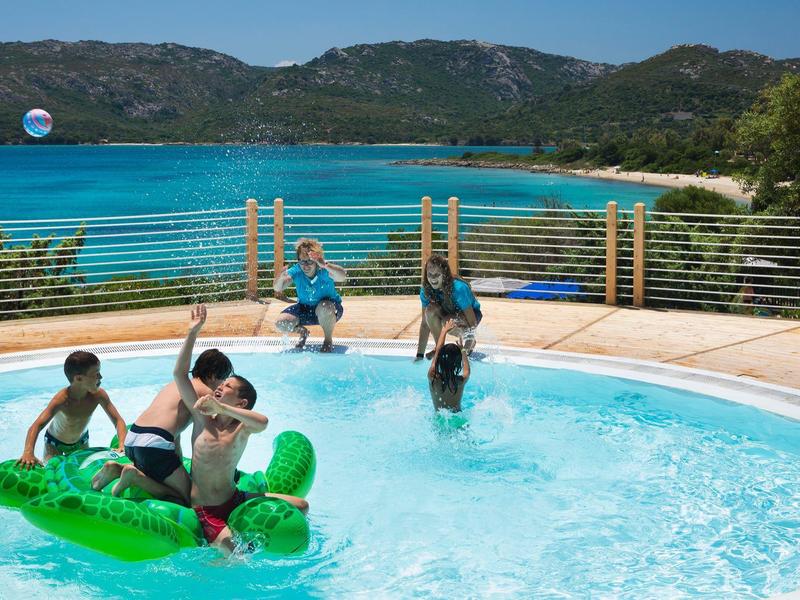Kinder spielen auf einem grünen Luftboot im Pool mit Berg- und Meerblick im Hintergrund.