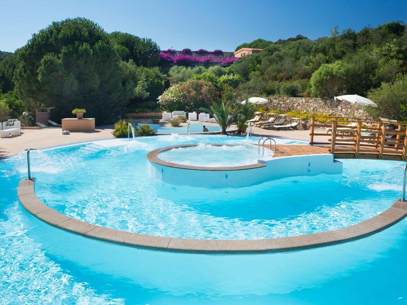 Schöner blauer Pool mit runden Inseln, Sitzbereich und grüner, bewaldeter Umgebung.