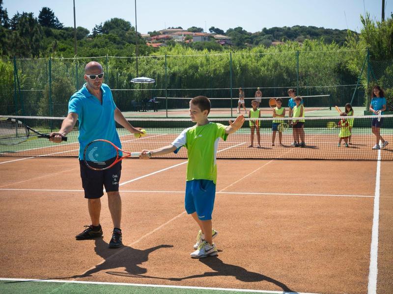 Zwei Jungen spielen Tennis auf einem Sandplatz, weitere Spieler im Hintergrund am Netz.