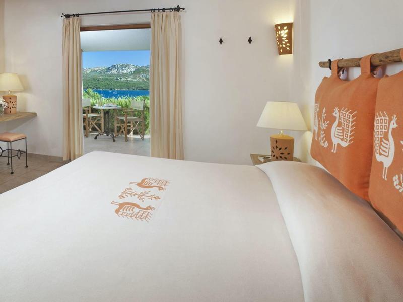 Helles Schlafzimmer mit großem Bett, weißen Wänden und Blick auf grüne Hügel durch offene Tür.