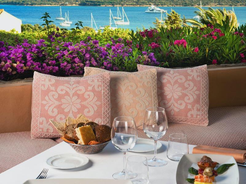 Gemütliche Terrasse mit rosa Kissen, gedecktem Tisch und Meerblick im Hintergrund.