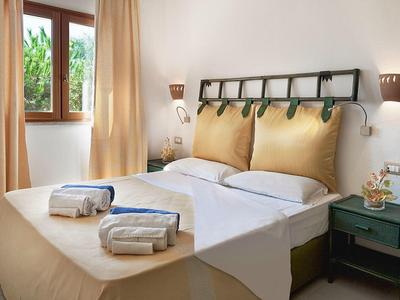 Hell eingerichtetes Schlafzimmer mit großem Bett, gepolstertem Kopfteil, zwei Handtüchern und grünem Nachttisch.