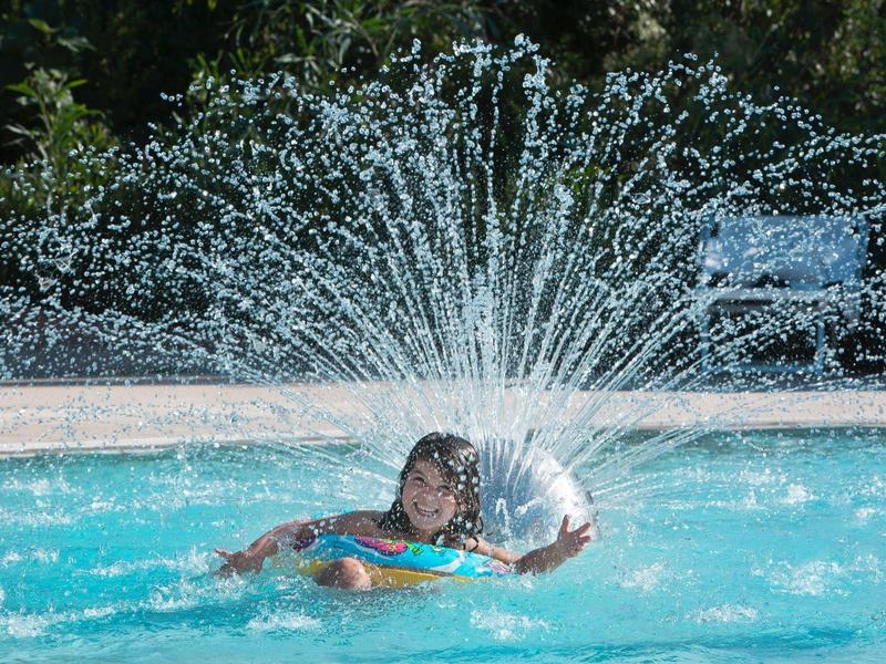 Frau im blauen Pool spielt mit spritzendem Wasser aus Springbrunnen im Hintergrund.